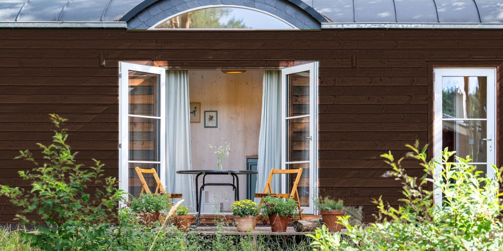 Tinyhaus mit dunkelbrauner Holzfassade, Tonnendach und geöffneter Terrassentür im Garten